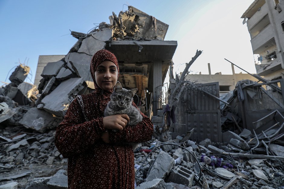 Палестинская девочка с кошкой в руках возле обломков разрушенного жилого дома после израильских авиаударов в Рафахе, сектор Газа, 18 октября 2023 года