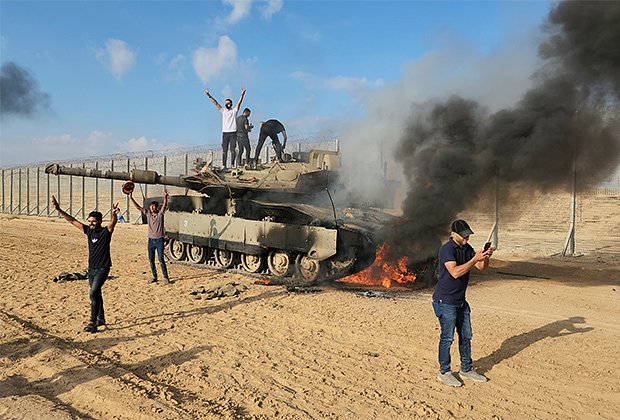Палестинцы около горящего израильского танка Merkava Mk 4, подбитого в ходе вторжения ХАМАС. 7 октября 2023 года
