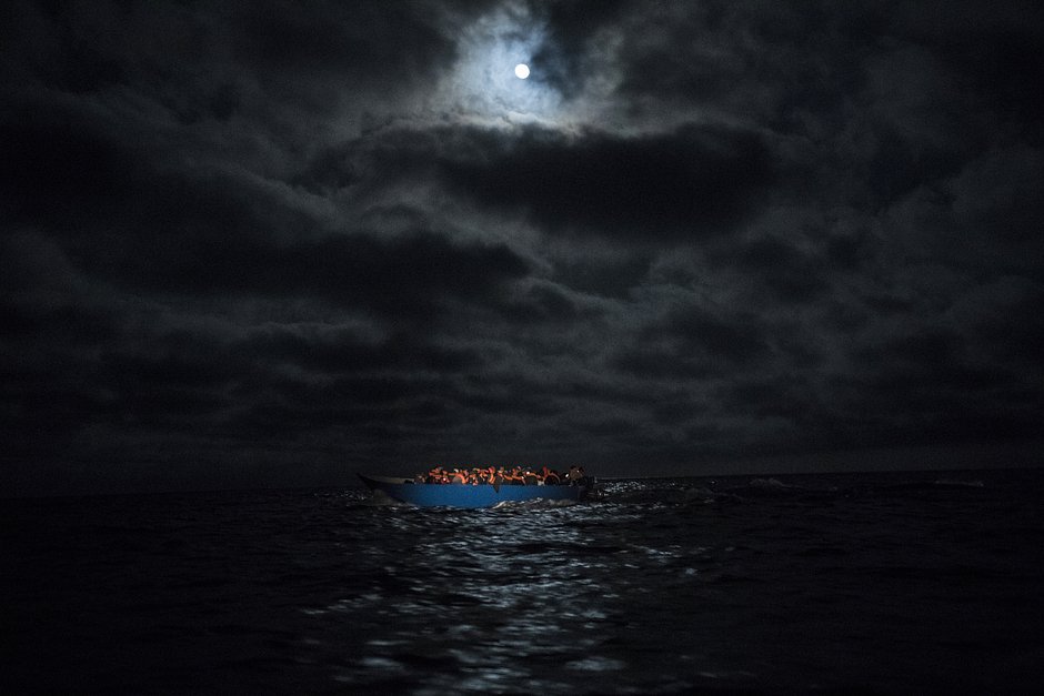 Деревянная лодка с мигрантами освещена прожектором спасателей из неправительственной организации Open Arms, Средиземное море, 29 марта 2021 года