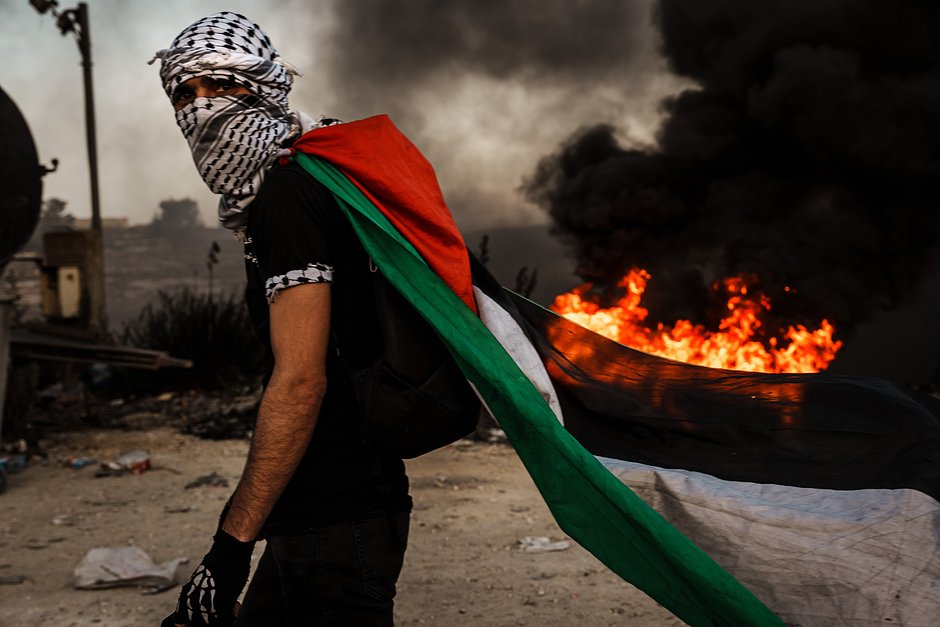 Житель Западного берега реки Иордан с палестинским флагом во время противостояния с израильскими правоохранителями в районе Бейт-Эль в Рамалле, 13 октября 2023 года