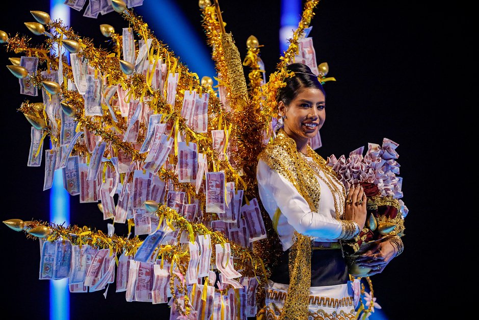 Фото с конкурса национальных костюмов «Мисс Вселенная — 2023». Костюм «Мисс Мьянмы» представляет вариацию на тему денежного дерева — традиционного подарка, который дарят молодым послушникам в день, когда они становятся буддийскими монахами.
