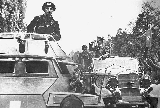 Адольф Гитлер приветствует салютующих солдат из своего автомобиля «Мерседес». На переднем плане — бронемашина SdKfz 222