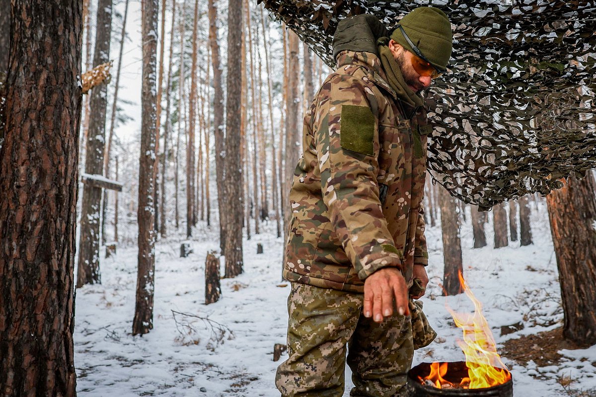 Военнослужащий Интернационального легиона территориальной обороны Украины греет руки у самодельной горелки неподалеку от линии фронта, 23 ноября 2023 года