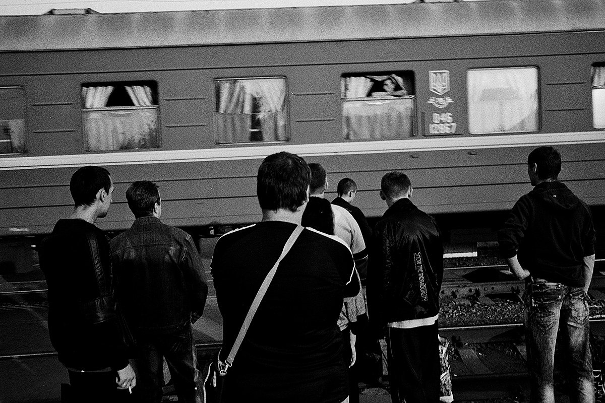 Подростки ждут, когда проедет проходящий поезд, у перекрытого железнодорожного переезда в одном из центральных кварталов города