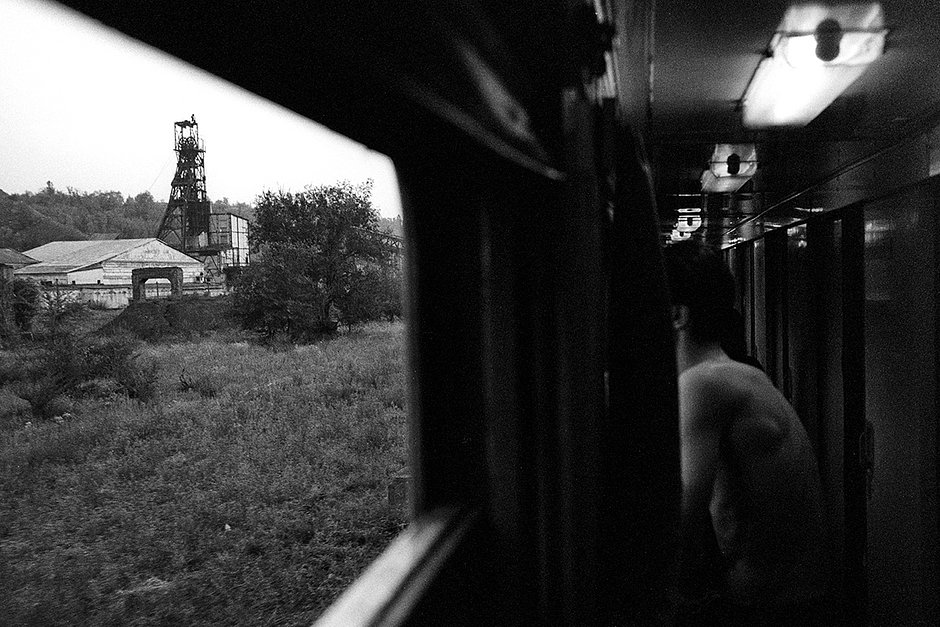 Молодой человек смотрит из купейного железнодорожного вагона на одну из шахт города