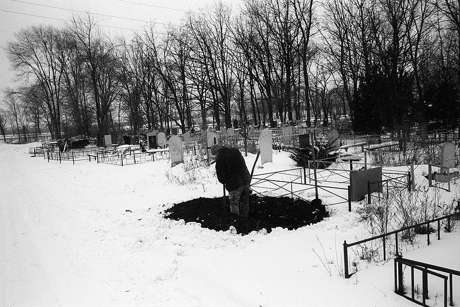 Гробокопальщик копает свежую могилу в промерзшей земле на городском кладбище