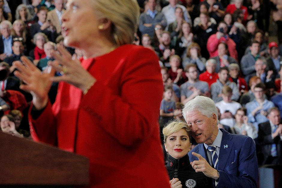 Бывший президент США Билл Клинтон и певица Леди Гага (на заднем фоне) разговаривают, в то время как кандидат в президенты США от Демократической партии Хиллари Клинтон выступает на предвыборном митинге в Роли, Северная Каролина, США, 8 ноября 2016 года