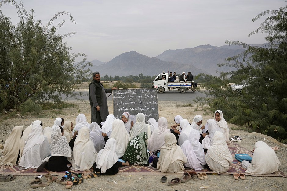 Афганские беженцы проходят мимо школы для девочек на открытом воздухе в Торкхаме, Афганистан, 18 ноября 2023 года