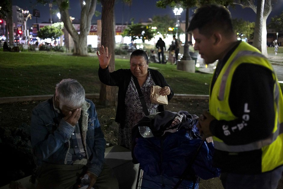 Церковные волонтеры Уильям Фимбрес (справа) и Лурдес Пуэрта (в центре) помогают Луису Каррильо, бездомному, живущему в парке Макартур в Лос-Анджелесе, 13 октября 2023 года