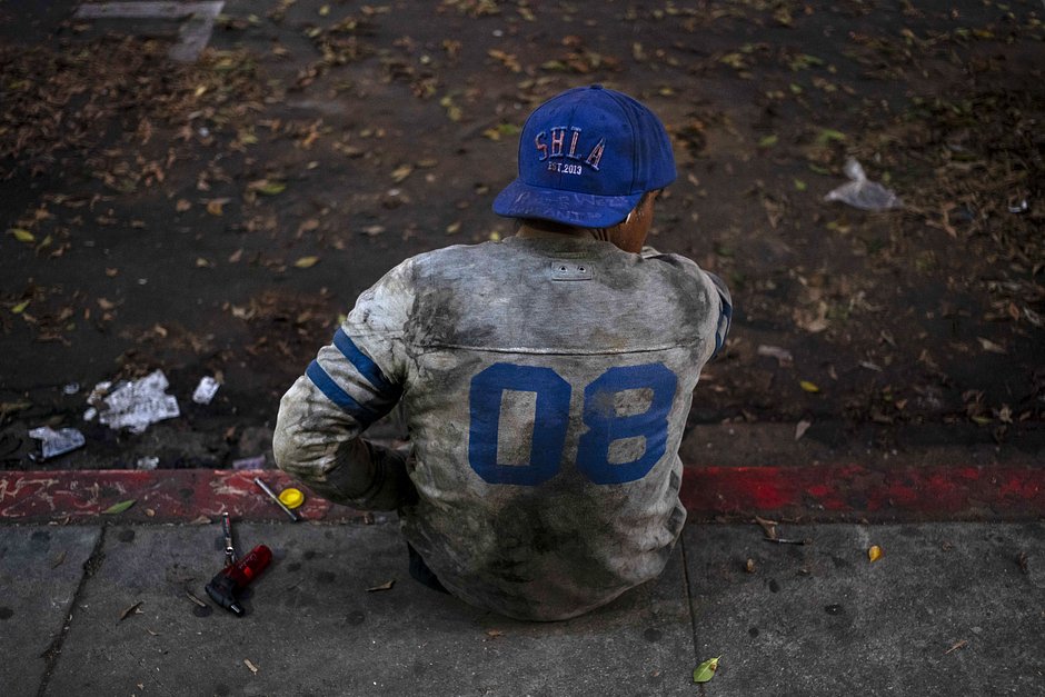 Бездомный в рваной спортивной форме на обочине улицы в Лос-Анджелесе, 20 октября 2023 года