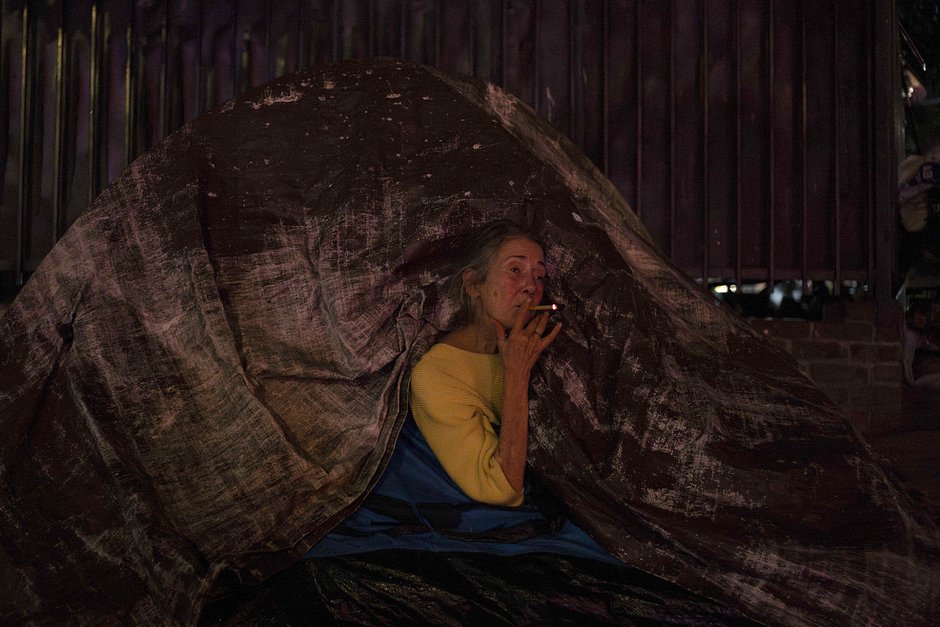Бездомная Патрисия Суини курит сигарету через щель в своей палатке, пока ее партнер спит внутри, Лос-Анджелес, 17 октября 2023 года
