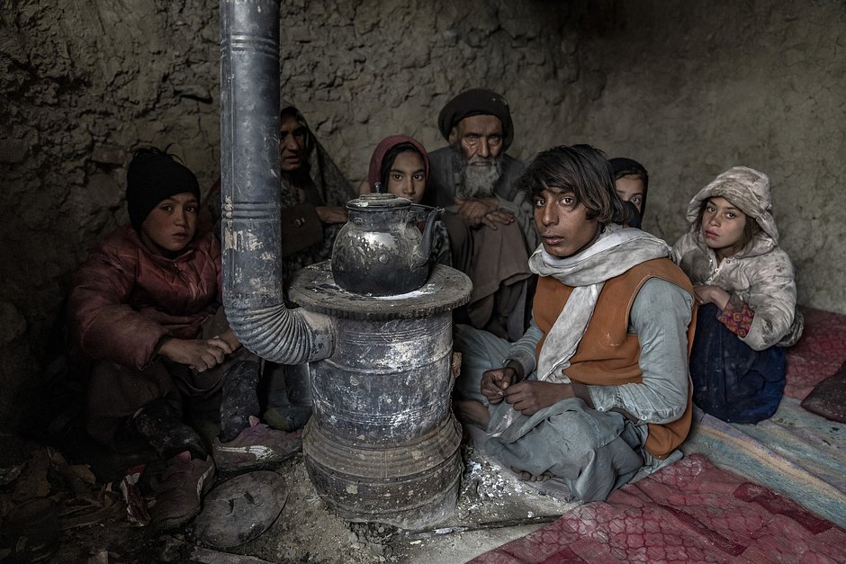 Семья вынужденных переселенцев ютится у печи, растопленной мусором в лагере на окраине Кабула, Афганистан, 10 января 2023 года