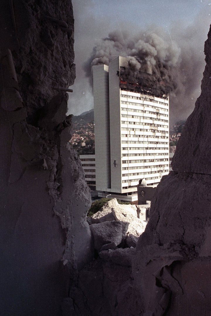 Здание парламента горит после попадания артиллерийского снаряда, вид из разрушенной гостиницы в центре Сараево, 20 августа 1992 года