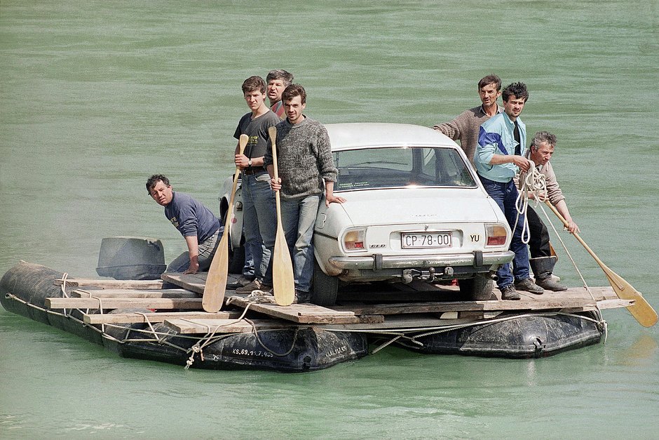 Беженцы используют импровизированный плот, чтобы переправить машину через реку Неретва после того, как армия взорвала мост, Босния и Герцеговина, 13 апреля 1992 года