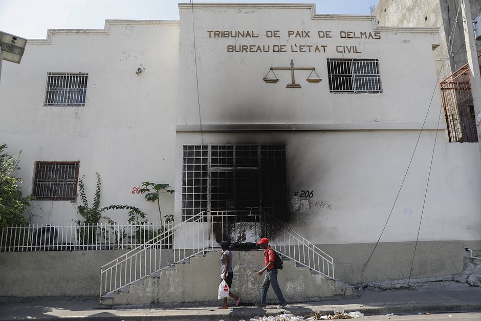 Пешеходы проходят мимо здания суда, подожженного бандитами в районе Дельмас, Порт-о-Пренс, Гаити, 6 марта 2024 года