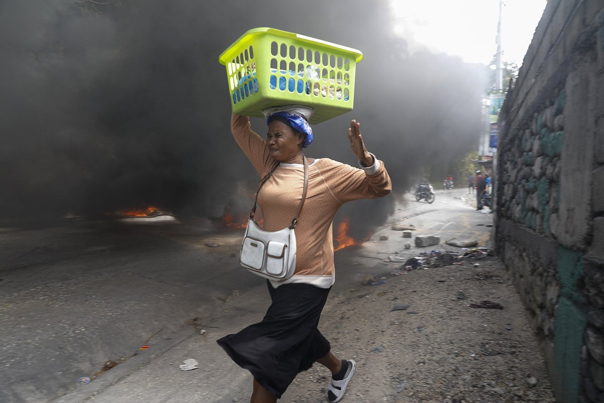 Женщина пробегает мимо горящих покрышек, подожженных участниками беспорядков, Гаити, 5 февраля 2024 года