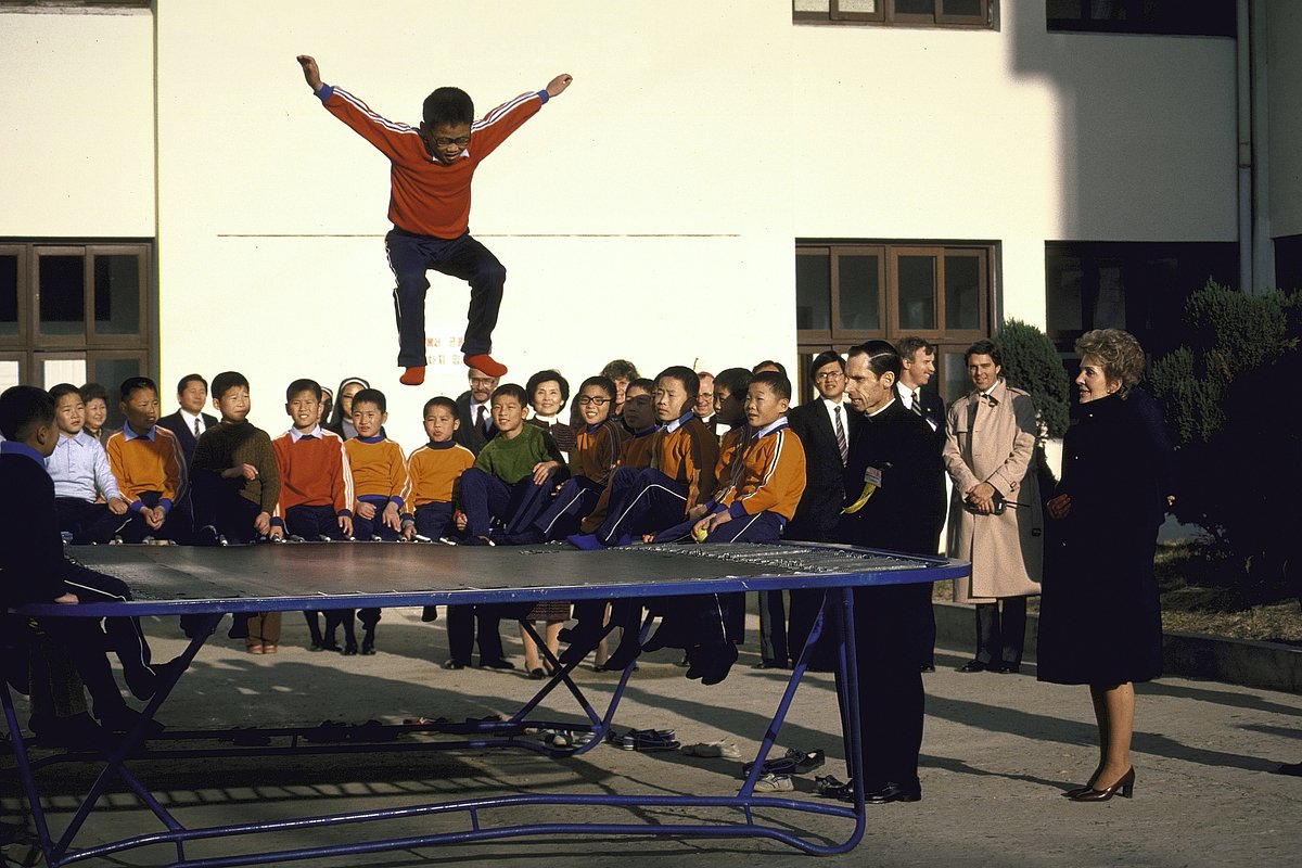 Демонстрация прыжков на батуте для первой леди США Нэнси Рейган (справа) во время ее визита в сеульский детский городок для сирот, Сеул, Республика Корея, 1 ноября 1983 года