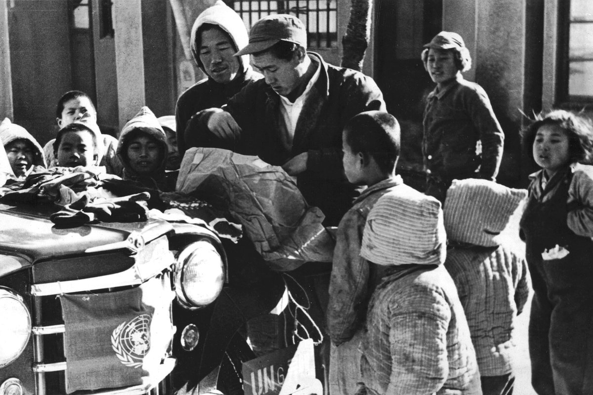 Корейская война, сироты собираются вокруг джипа ООН, чтобы изучить содержимое посылок, отправленных иностранными детьми, 1950-1953 годы 