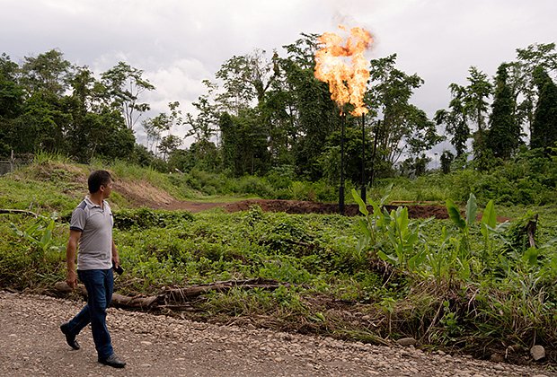 Мужчина идет рядом с языками пламени, вырывающимися из горелки на заводе государственной нефтяной компании Petroecuador в Лаго-Агрио, Эквадор