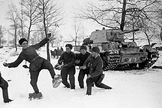 Бойцы Сталинградского фронта со смехом примеряют трофейную обувь немецких солдат из соломы, которая надевалась поверх кожано-войлочных бот. Справа — танк КВ-1