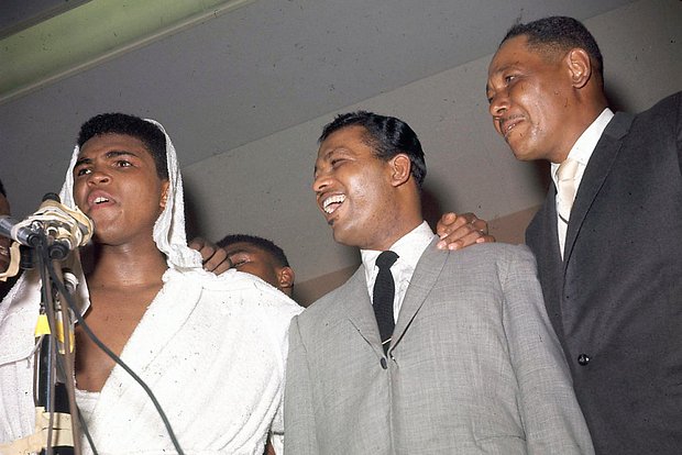 Cassius Clay holds court after his bout with Sonny Liston in Miami Beach, Fla., Feb. 25, 1964. With him is Sugar Ray Robinson. Man at far right is unidentified