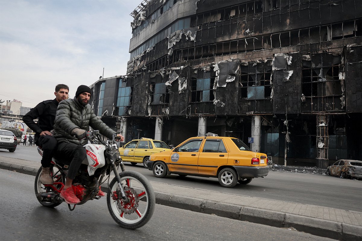 People ride a motorbike near a burnt building of the Department of Immigration and Passports which was managed by the Syrian Ministry of Interior, after rebels seized the capital and ousted Syria's Bashar al-Assad