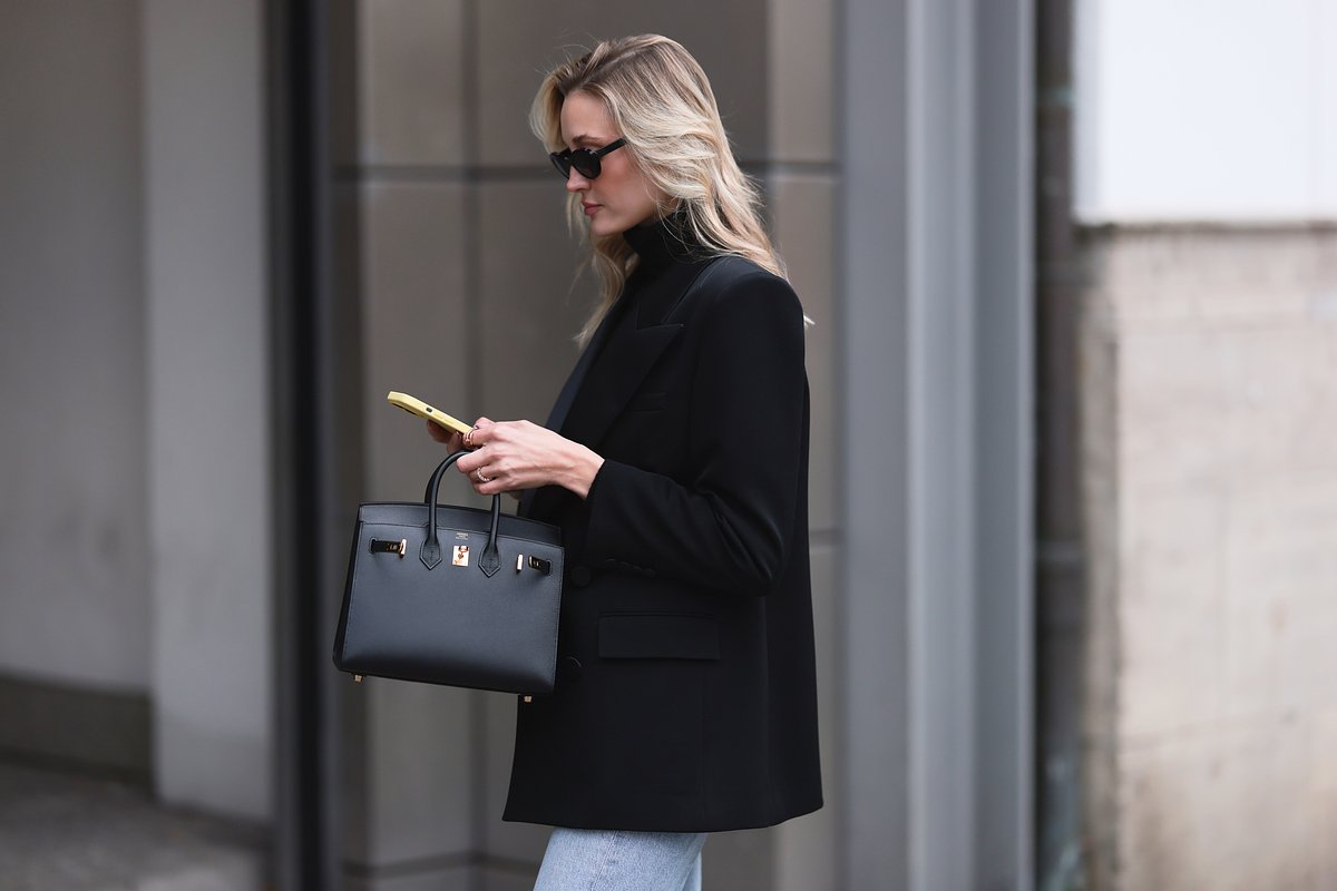 Манди Борк в черном пиджаке Saint Laurent и черной водолазке Liu Jo, голубых джинсах Agolde, закругленных очках Chanel, с черной кожаной сумкой Hermes Birkin