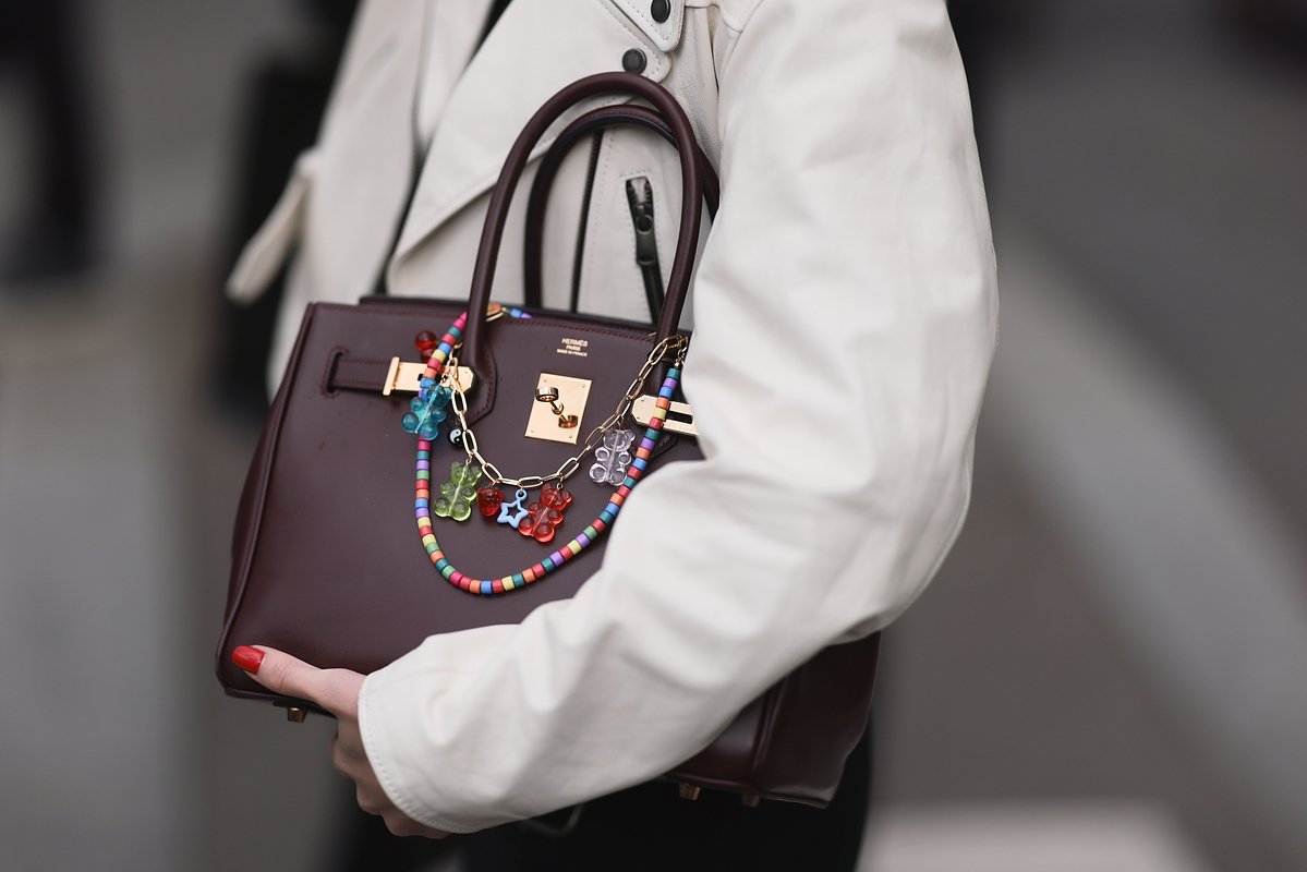 Гостья в коротком плаще из белой кожи и с сумкой Hermès birkin бордового цвета с цветными цепочками во время показа женской коллекции осень-зима 2024/2025 от Miu Miu в рамках Недели моды в Париже
