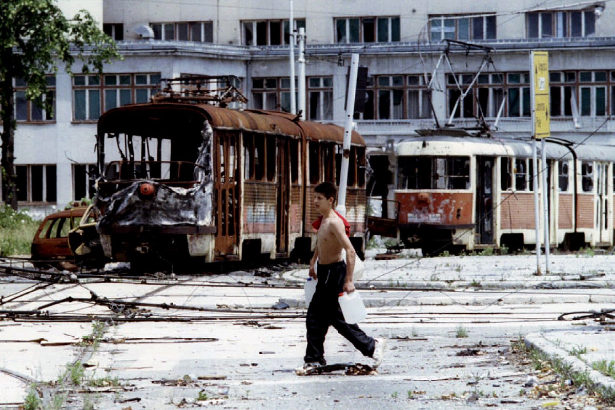 Боснийский подросток проходит мимо разрушенных трамваев на площади Скендерия в осажденной боснийской столице Сараево, 22 июня 1993 года