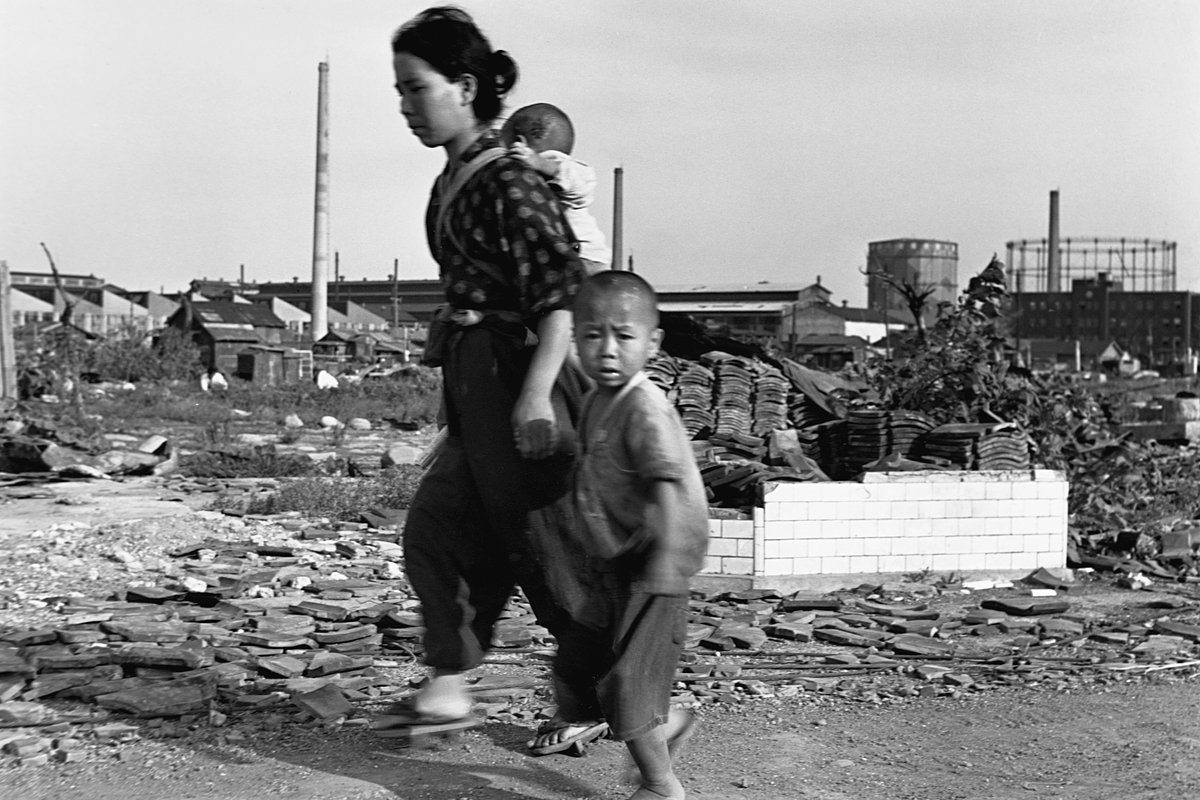 Японская женщина с детьми идут по заваленной обломками улице в Токио, Япония, 1945 год