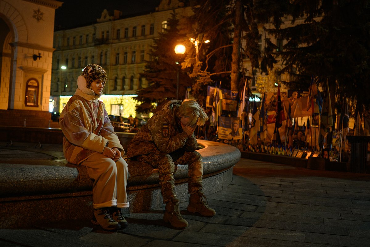 Военнослужащий Вооруженных сил Украины сидит девушкой у мемориала украинским и иностранным солдатам на площади Независимости во время отключения электроэнергии в Киеве, 25 ноября 2025 года
