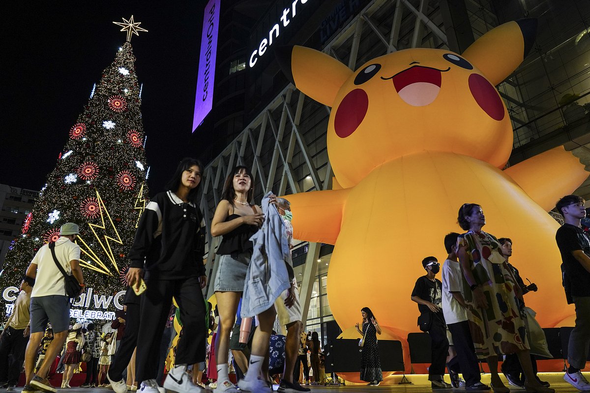 Люди фотографируются на фоне большой освещенной рождественской елки и надувной куклы Пикачу в столице Таиланда Бангкоке 31 декабря 2023 года