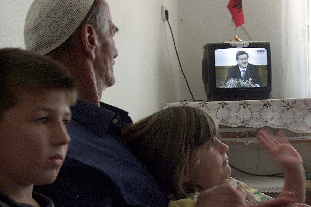 Беженцы албанского происхождения смотрят выступление генерального секретаря НАТО Джорджа Робертсона по телевидению 14 июня 2001 года, в то время как поток беженцев албанского происхождения из Македонии продолжался