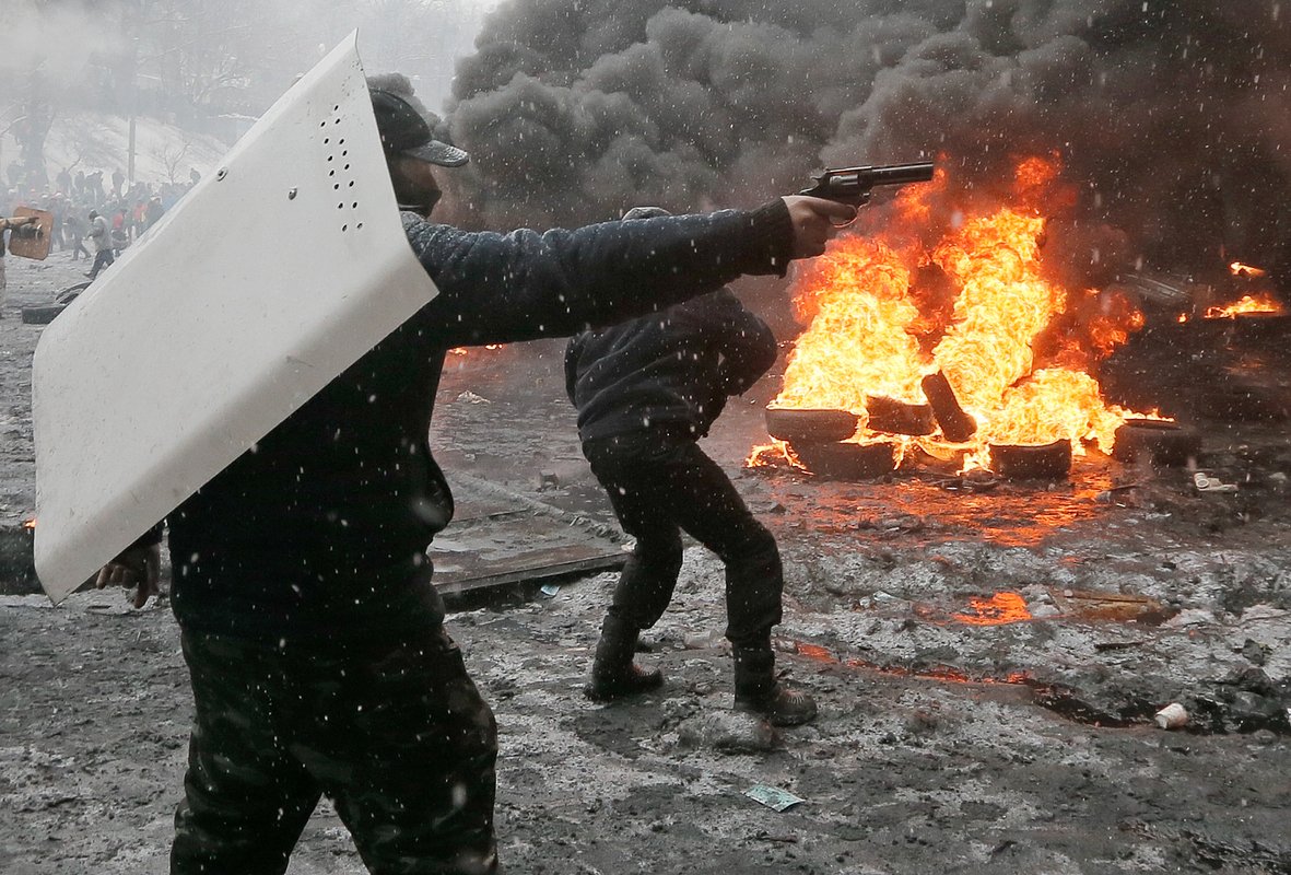 Протестующий направляет пистолет в силовика во время столкновения с полицией в центре Киева, Украина, 22 января 2014 года