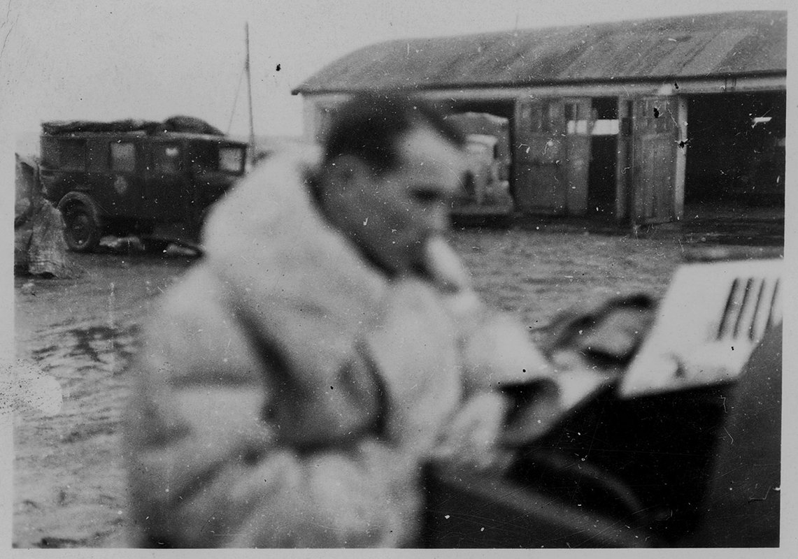 Немецкий офицер у гаража с автомобилями вермахта. На фоне видны автомобиль и антенна радиосвязи СССР. 1941 год