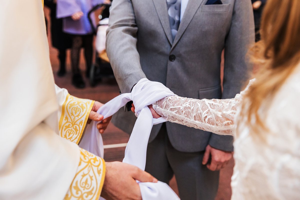 При обручении пары священник символически связывает руки венчающихся рушником 