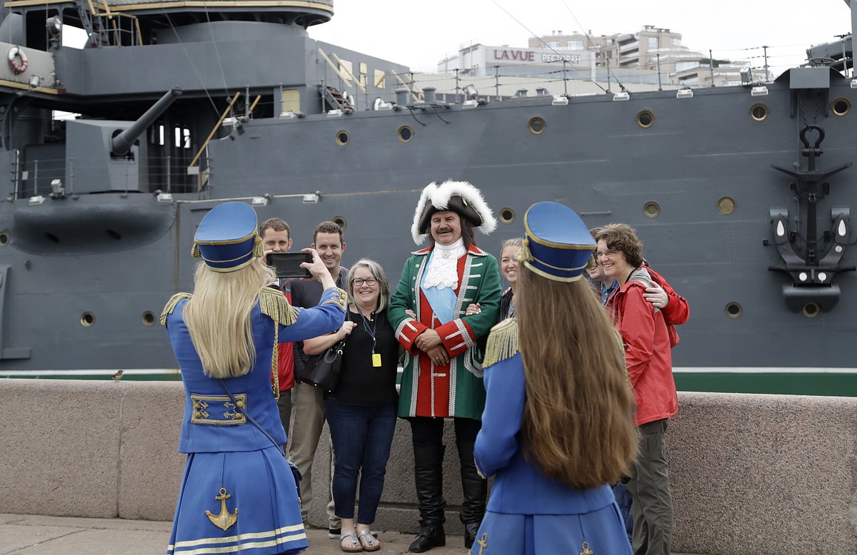 Tourists pose for a photo in front of the Aurora cruise ship during the 2018 soccer World Cup in St. Petersburg, Russia, Monday, July 9, 2018